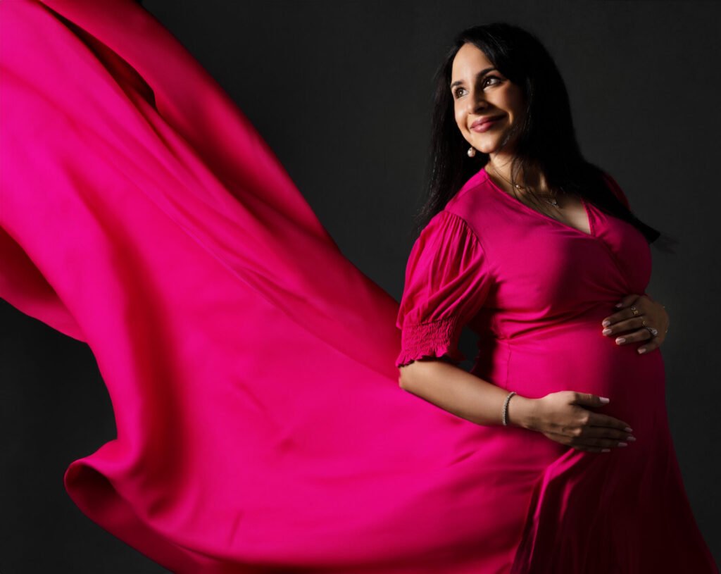 Maternity portrait in studio with soft lighting and neutral background, showing expecting mother smiling